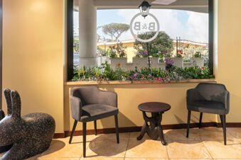Two gray armchairs and a small dark table are placed near a window with a planter box at B&B Hotel Pomezia Cortese