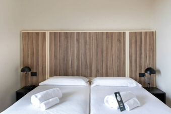 Two single beds with white sheets, rolled towels, black reading lamps, and wooden panel headboards at B&B Hotel Pomezia Cortese
