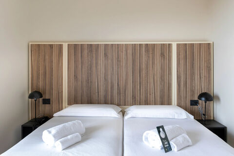 Two single beds with white sheets, rolled towels, black reading lamps, and wooden panel headboards at B&B Hotel Pomezia Cortese