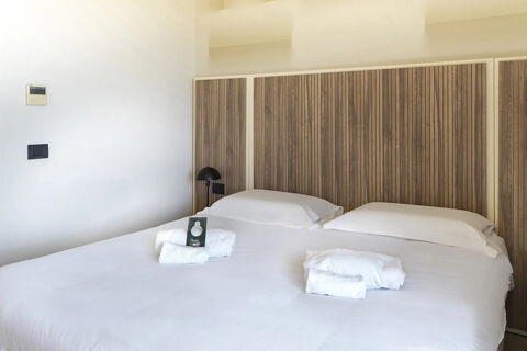 A double bed with white bedding, wooden panel headboard, two pillows, two sets of folded towels, and a black bedside lamp in B&B Hotel Pomezia Cortese