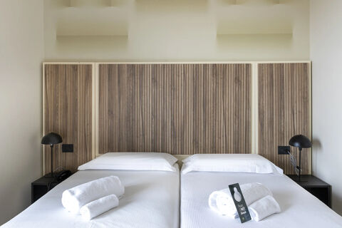Two single beds with white linens and rolled towels with a "Do Not Disturb" sign in B&B Hotel Pomezia Cortese