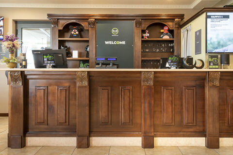 Reception desk with key hooks, computer monitors, decorative items, and a welcome sign at B&B Hotel Pomezia Cortese