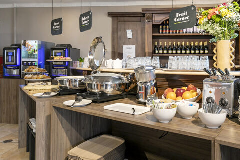 Breakfast buffet area at B&B Hotel Pomezia Cortese with plates, fruit, juice dispenser, toaster, glasses, and pastries displayed