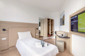 Single bed with white linens and towels, open wardrobe, wall-mounted TV, and desk in B&B Hotel Pomezia Roma room