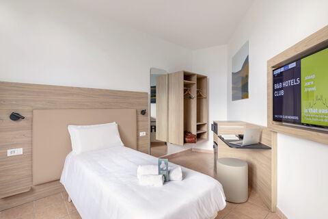 Single bed with white linens and towels, open wardrobe, wall-mounted TV, and desk in B&B Hotel Pomezia Roma room