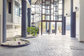 Modern hotel entrance area with large black columns, glass walls, decorative plants, and stone tile flooring at B&B Hotel Pomezia Roma