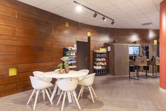 Interior of B&B Hotel Pomezia Roma with a round white table, five modern chairs, wooden walls, and snack racks in the background