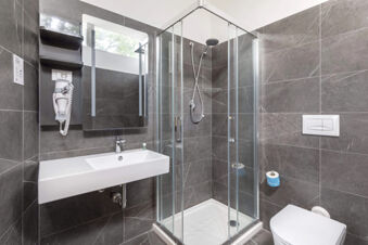 Modern bathroom with glass shower cabin, white sink, wall-mounted hairdryer, toilet, and gray marble tiles at B&B Hotel Pomezia Roma