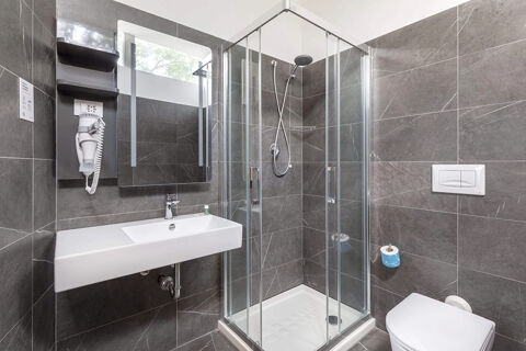 Modern bathroom with glass shower cabin, white sink, wall-mounted hairdryer, toilet, and gray marble tiles at B&B Hotel Pomezia Roma