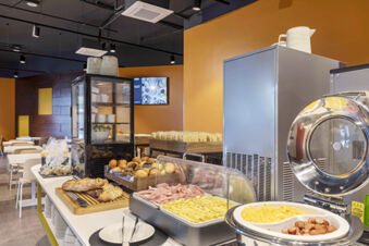 Breakfast buffet with bread, cold cuts, cheese, scrambled eggs, sausages, and packaged snacks at B&B Hotel Pomezia Roma