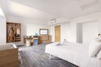 Bright hotel room at B&B Hotel Pomezia Roma with a large bed, wooden furniture, open closet, and TV on the wall