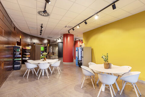 Interior view of B&B Hotel Pomezia Roma with white tables and chairs, yellow wall, red columns, and vending machines visible