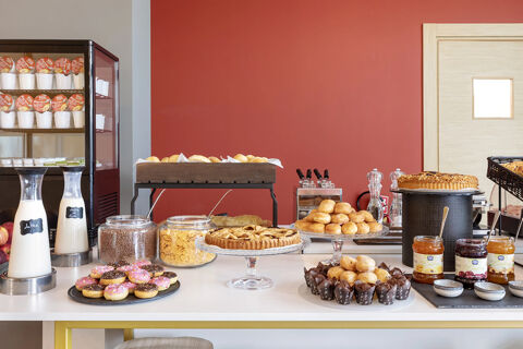 A breakfast buffet at B&B Hotel Roma Fiumicino Aeroporto Fiera 2 with pastries, jars of cereal, milk bottles, and jars of jam on a white table