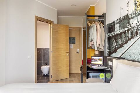 Hotel room at B&B Hotel Roma Fiumicino Aeroporto Fiera 2 with a bed, open doors, hanging clothes, laptop, and a bidet in the bathroom visible