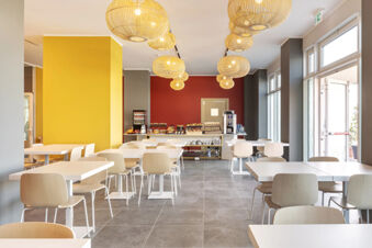 Dining area at B&B Hotel Roma Fiumicino Aeroporto Fiera 2 with white tables, wooden chairs, hanging light fixtures, and a buffet station