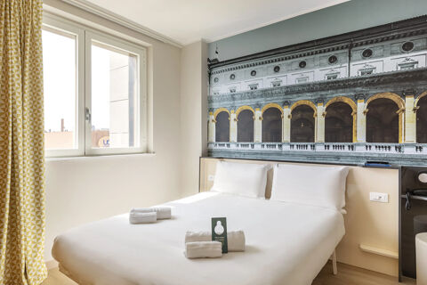 Bright hotel room at B&B Hotel Roma Fiumicino Aeroporto Fiera 2 with double bed, white linens, window, and yellow-patterned curtains