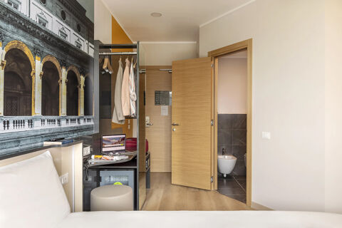 Hotel room interior at B&B Hotel Roma Fiumicino Aeroporto Fiera 2 with bed, open closet, desk, and bathroom door visible
