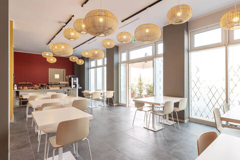 Bright dining area with white tables, wooden chairs, hanging wicker lamps, and a buffet counter at B&B Hotel Roma Fiumicino Aeroporto Fiera 2