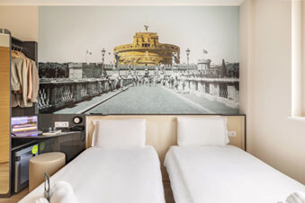Hotel room at B&B Hotel Roma Fiumicino Aeroporto Fiera 2 with two single beds, a large wall art, and a small work desk area