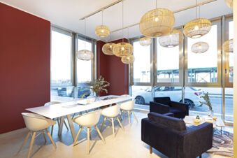 Bright meeting room at B&B Hotel Roma Fiumicino Aeroporto Fiera with white chairs around a table and black armchairs near windows