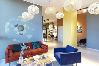 Modern hotel lounge at B&B Hotel Roma Fiumicino Aeroporto Fiera with orange couch, blue armchair, and decorative wall art