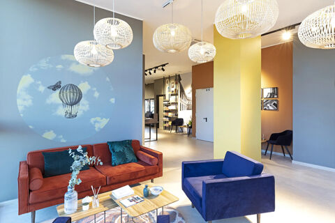 Modern hotel lounge at B&B Hotel Roma Fiumicino Aeroporto Fiera with orange couch, blue armchair, and decorative wall art
