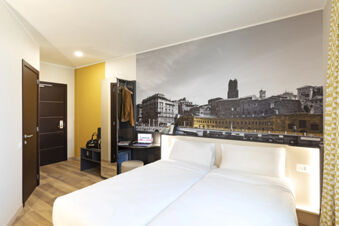 Modern hotel room at B&B Hotel Roma Fiumicino Aeroporto Fiera with two white beds, wooden floor, and a large cityscape mural on the wall
