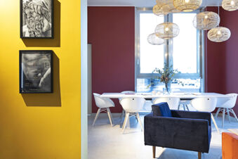 Interior of B&B Hotel Roma Fiumicino Aeroporto Fiera with yellow and maroon walls, white chairs, blue armchair, and hanging lamps