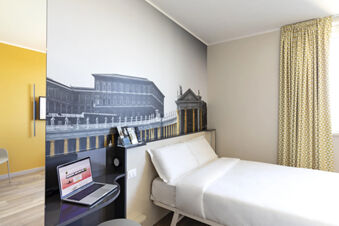 Hotel room at B&B Hotel Roma Fiumicino Aeroporto Fiera with white bed, black and white wall mural, and patterned yellow curtains