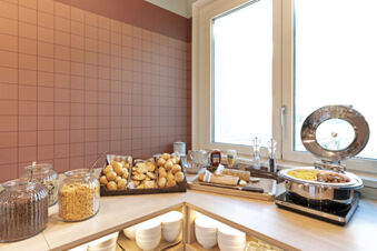 Breakfast buffet with cereals, various breads, condiments, and hot food near a window at B&B Hotel Roma Fiumicino Aeroporto Fiera