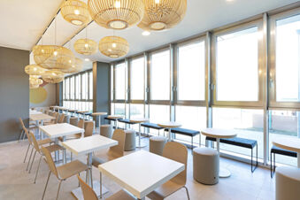 Bright dining area at B&B Hotel Roma Fiumicino Aeroporto Fiera with white tables, wooden chairs, and round pendant lights