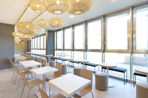 Bright dining area at B&B Hotel Roma Fiumicino Aeroporto Fiera with white tables, wooden chairs, and round pendant lights