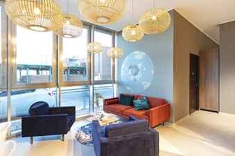 Living room seating area with blue and orange couches, wooden pendant lights, and wall art at B&B Hotel Roma Fiumicino Aeroporto Fiera