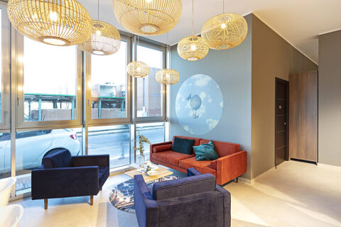 Living room seating area with blue and orange couches, wooden pendant lights, and wall art at B&B Hotel Roma Fiumicino Aeroporto Fiera