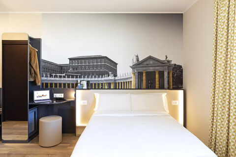 Hotel room at B&B Hotel Roma Fiumicino Aeroporto Fiera with a white bed, mural of classical buildings, desk, and patterned curtains