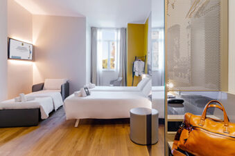 Bright hotel room at B&B Hotel Roma Pietralata Tiburtina with two beds, a small armchair, wooden floor, and a window