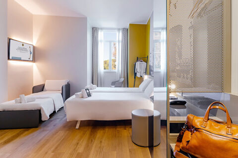 Bright hotel room at B&B Hotel Roma Pietralata Tiburtina with two beds, a small armchair, wooden floor, and a window
