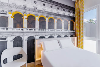 Modern hotel room at B&B Hotel Roma Pietralata Tiburtina with a white bed, white chair, large wall mural, and yellow curtains