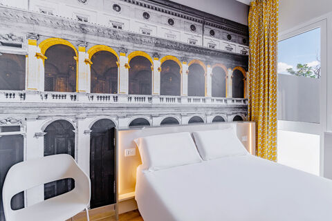 Modern hotel room at B&B Hotel Roma Pietralata Tiburtina with a white bed, white chair, large wall mural, and yellow curtains