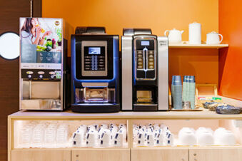 Coffee machines, tea cups, glasses, and disposable cups displayed on a light wooden counter at B&B Hotel Roma Pietralata Tiburtina
