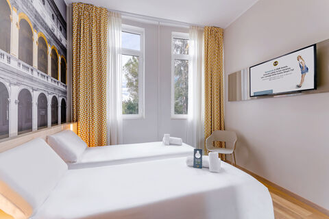 Two neatly made single beds with white linens and rolled towels in a bright room at B&B Hotel Roma Pietralata Tiburtina