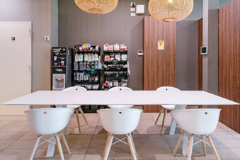White table with six white chairs on tiled floor under two rattan pendant lights near a vending machine at B&B Hotel Roma Pietralata Tiburtina