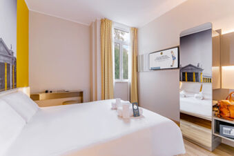 Modern hotel room at B&B Hotel Roma Pietralata Tiburtina with a large bed, folded towels, and a wall-mounted TV