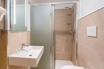 Bathroom sink with soap and shampoo bottles next to a shower cabin with glass doors at B&B Hotel Roma Pietralata Tiburtina