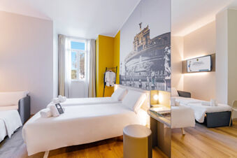 Bright hotel room with two single beds, a sofa, yellow accent wall, large window, and wall art at B&B Hotel Roma Pietralata Tiburtina