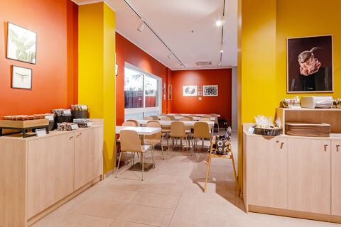 Dining area with wooden chairs and tables, bright yellow and orange walls, snack counter at B&B Hotel Roma Pietralata Tiburtina