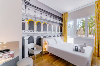 B&B Hotel Roma Pietralata Tiburtina room with double bed, white linens, wall art, yellow patterned curtains, and natural light from windows