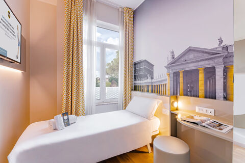 Small hotel room with single bed, large window with yellow patterned curtains, wall art, and TV at B&B Hotel Roma Pietralata Tiburtina