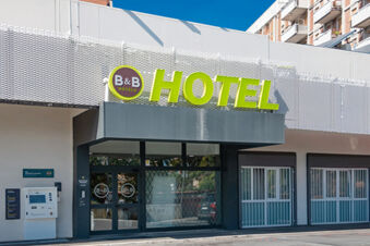 Entrance of B&B Hotel Roma Pietralata Tiburtina with bright green hotel sign above glass doors and white barred windows next to it