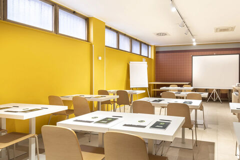 Meeting room with white tables, wooden chairs, yellow walls, a flipchart, and a projector screen at B&B Hotel Roma San Lorenzo Termini